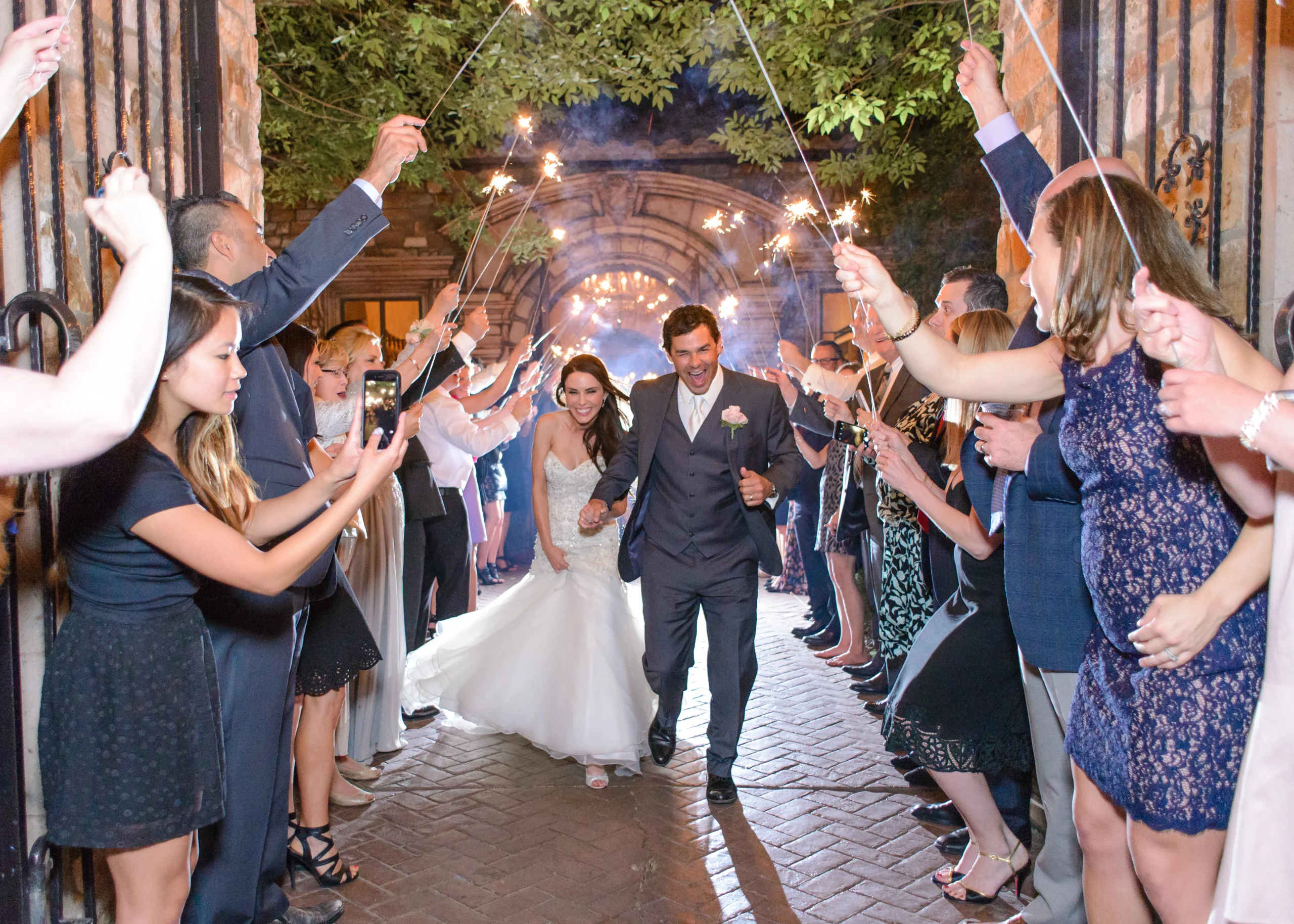 A newly married couple walks out through a sparkler send off as guests cheer.